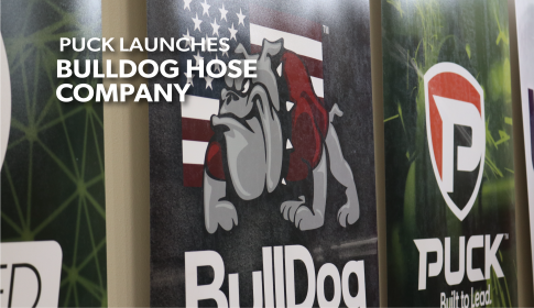 banners hanging in the Puck lobby, the ones displayed are BullDog Hose Company in the center and Puck Enterprises on the right. the overlaid title reads Puck Launches BullDog Hose Company