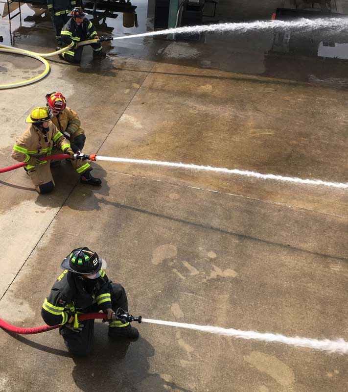 three firefighters crouching and holding hoses