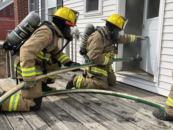 two Tripoli firefighters crouching with the Hi-Combat II attack hose and preparing to enter a smoky house