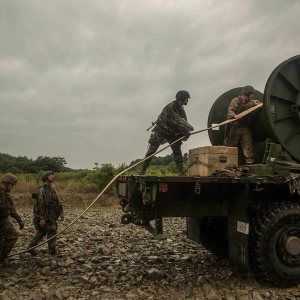 Marines standing on the back of a truck unrolling a fuel hose
