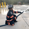 a side view of a firefighter crouching and using a blue hose to spray water