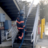 a firefighter walking up exterior stairs and shooting water from a blue hose