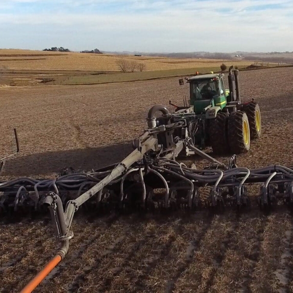 a tractor moving through a field with a pull-type toolbar and dragline hose being pulled behind it