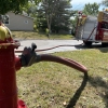 a fire hydrant with a wrench sitting on top and a U.S. Coupling manifold attached to an arm with the crank open to allow water into the Red Chief hose connected. in the background the hose is also connected to the fire truck and curls with no kinks on the street ground