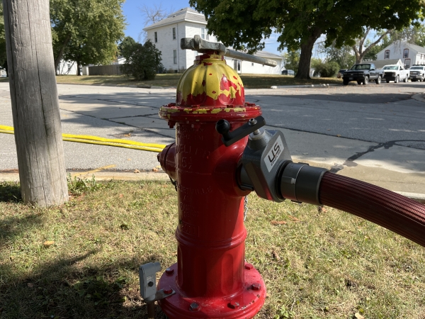 a fire hydrant with a wrench sitting on top and a U.S. Coupling manifold attached to an arm with the crank open to allow water into the Red Chief hose connected