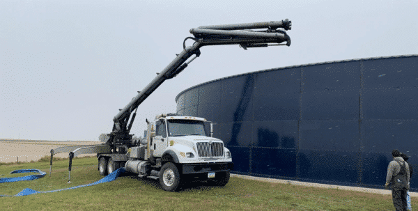 boom truck manure pump unit parked next to a manure pit with the arm extending over the side of the pit