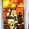 the backside of two firefighters holding the Hi-Combat II hose in the entryway of a building that is on fire