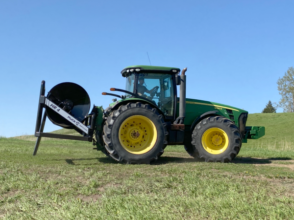 side view of a tractor and a Puck HR 4 3PT hose reel on a tractor with black hose on the reel