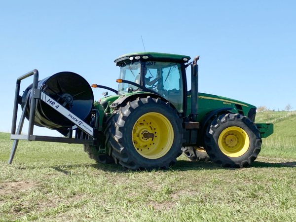 a side view of a Puck HR 4 3PT hose reel on a tractor with black hose on the reel