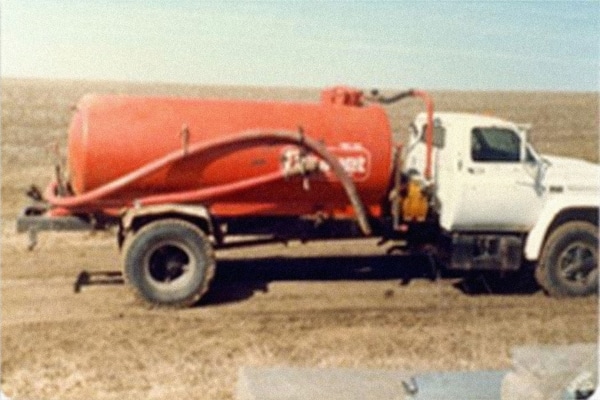 a white truck with a red drum on the bed in the fields in 1979