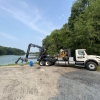 a boom truck parked and stabilized next to water with a blue hose rolled up next to the truck and ready to use