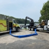 a fire truck and boom truck connected via a blue hose while parked next to the water