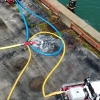 five hoses connected to a manifold with a cage on one end to catch the foam pigging ball when it reaches the end of the line, water is rushing out of the cage as the line is cleared