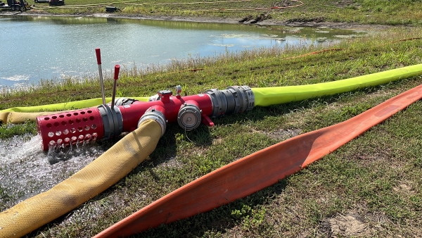 a U.S. Coupling manifold and attached pig catcher on the ground with hoses attacked next to a pond. the cage has water pouring out from the line being purged