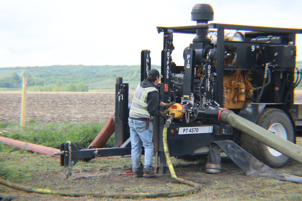a man in a hi vis vest attaching air hose to a pump trailer in the field