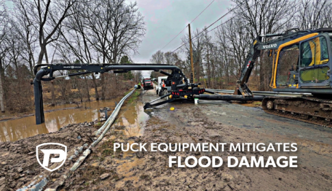 a Force Feed trailer parked next to a damaged guardrail with the hydraulic boom reaching into the flooded ditch to pump water out with the overlaid title reading Puck Equipment Mitigates Flood Damage